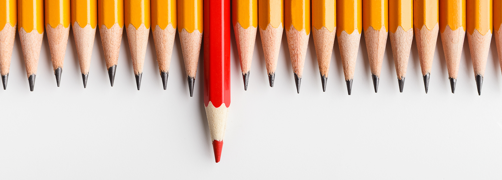 Mehrere Bleistifte in einer Reihe ein roter Buntstift herausragend außergewöhnlich