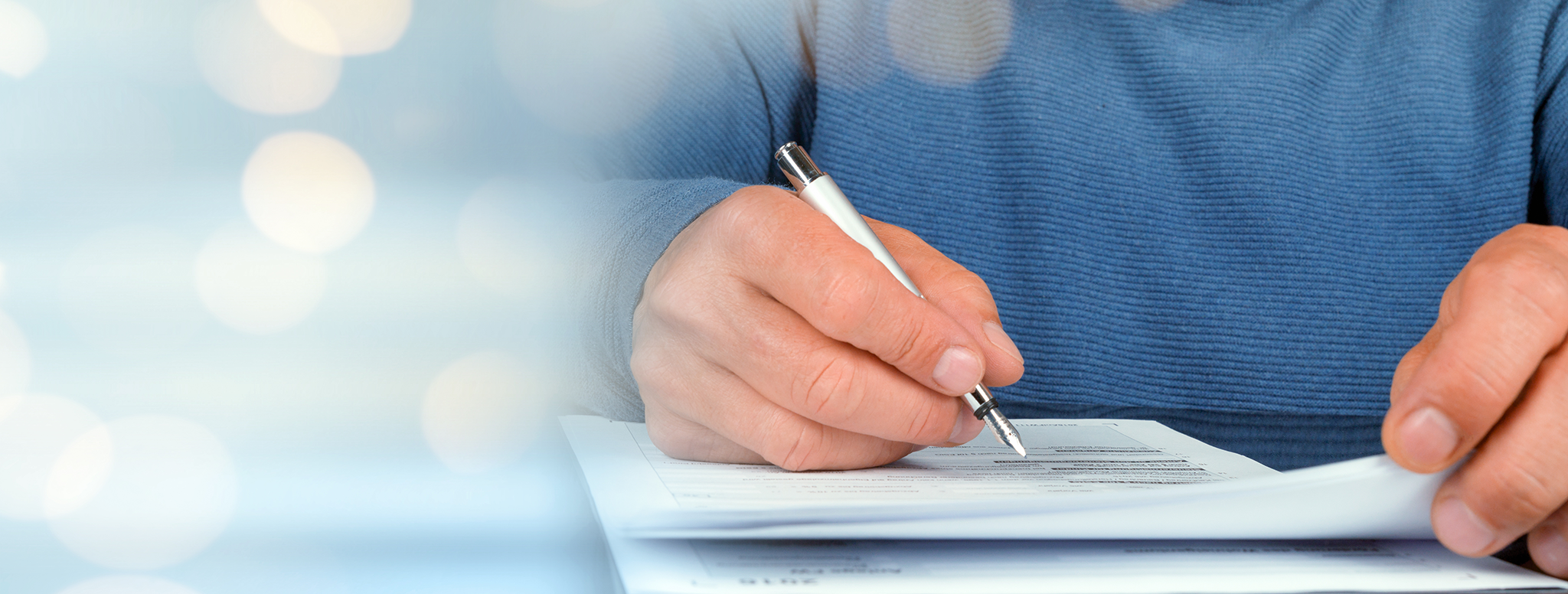 Mann im blauen Pullover am Schreibtisch mit Füller in der Hand überprüft Lücken im Lebenslauf